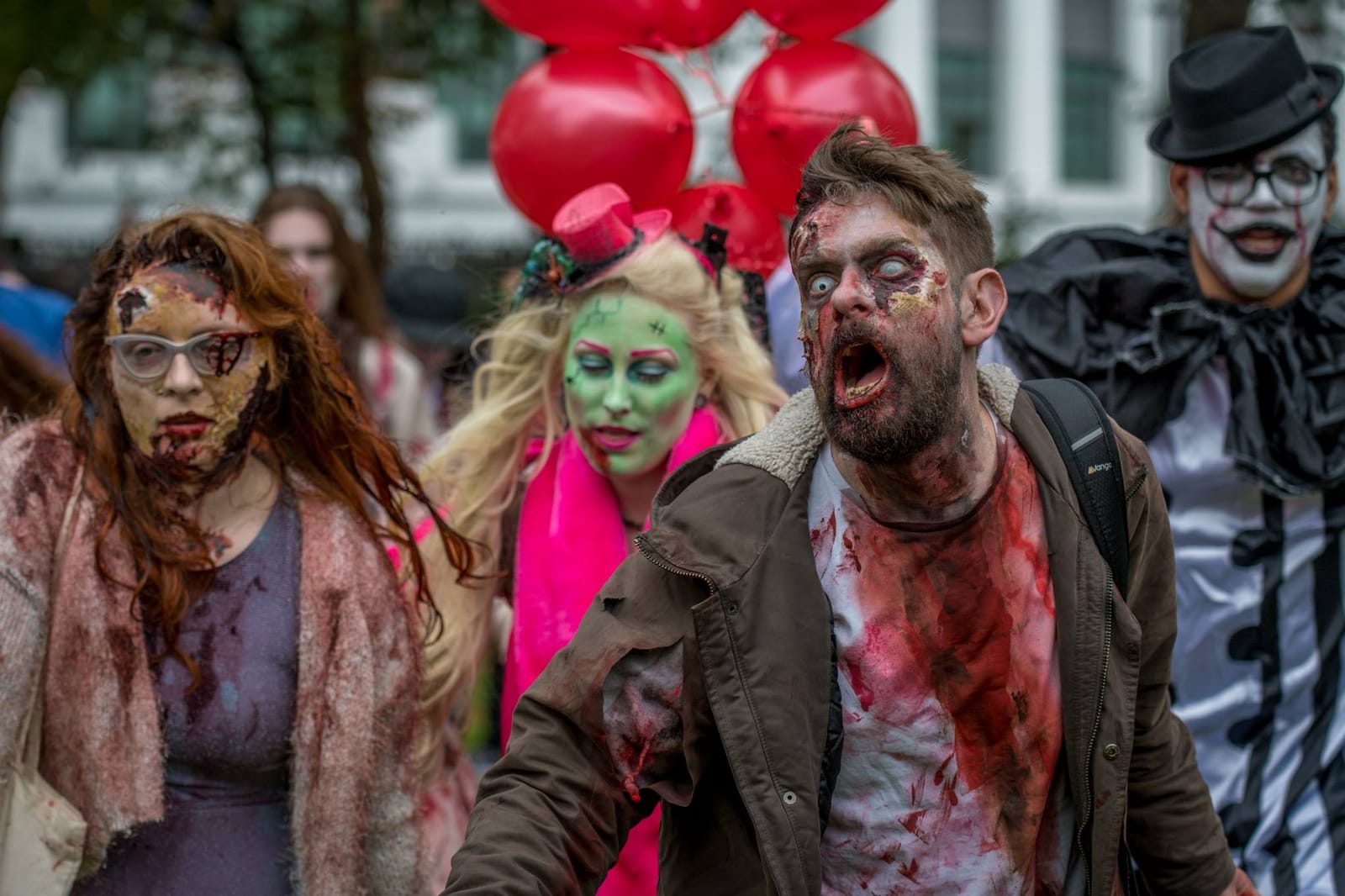A group of zombies advances towards the camera past a cluster of red balloons, one man caught mid-groan.