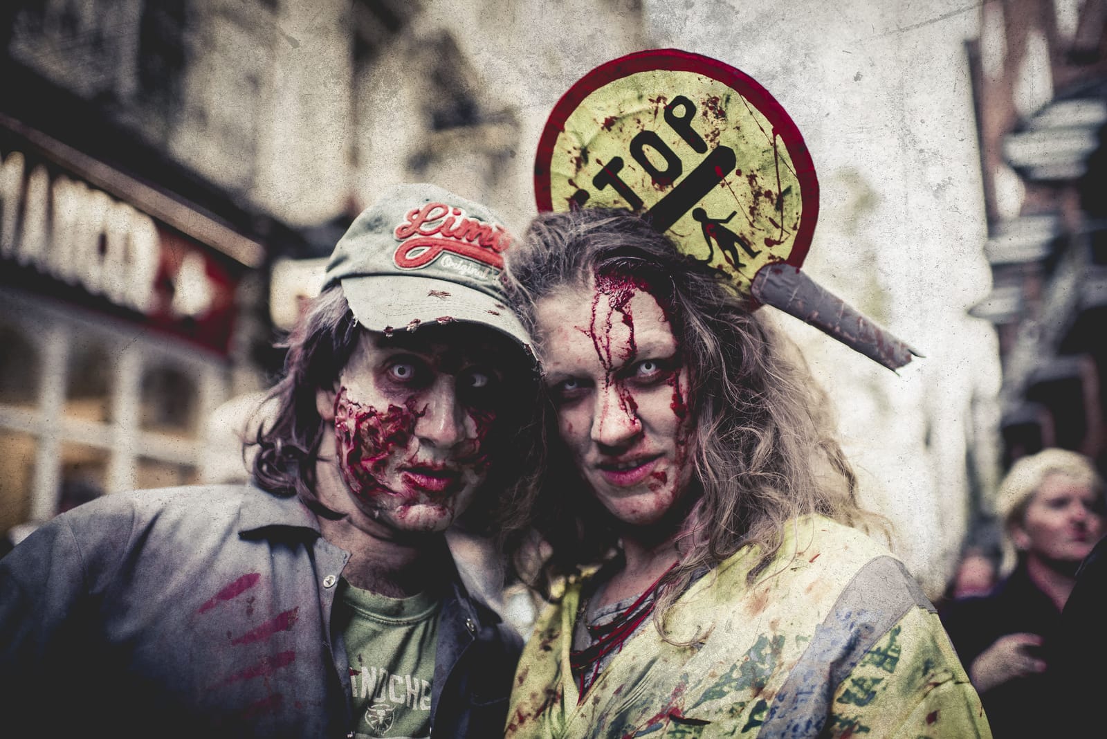 Two zombies pose cheek to cheek in the street, one wearing a prop road sign speared through the head.