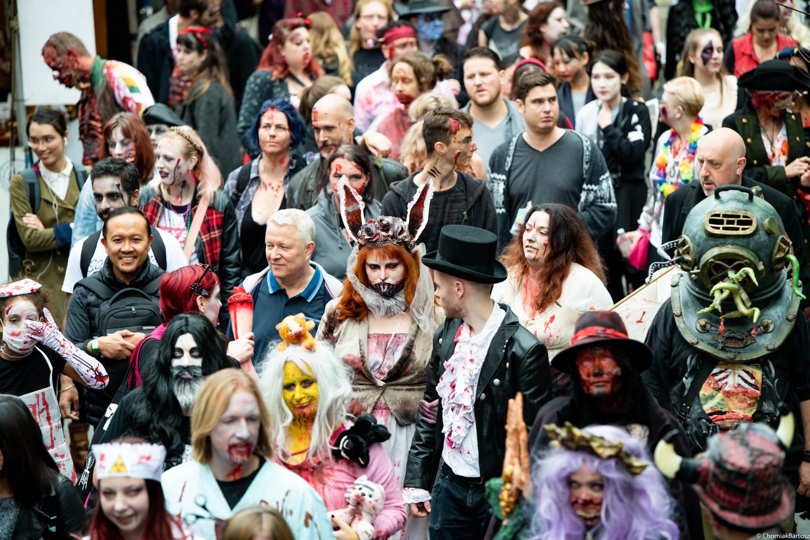 Hundreds of costumed zombies packed into a London street, photographed from above, a bride with rabbit ears, a deep-sea diving helmet, top hats and hospital scrubs among them.